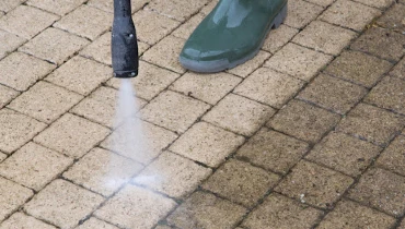 A handyman pressure washing an outdoor surface made of stone tiles, with a clear contrast between the clean area and the older, grimey area.