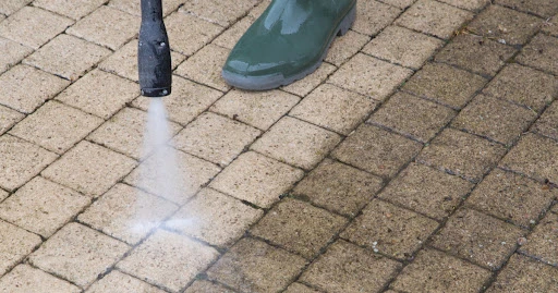 A handyman pressure washing an outdoor surface made of stone tiles, with a clear contrast between the clean area and the older, grimey area.