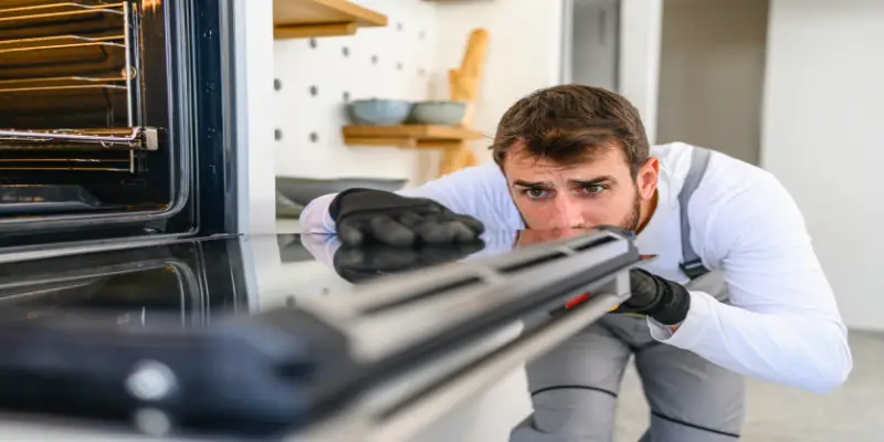 A technician/handyman repairs and cleans an oven door.