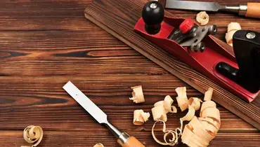 A closeup of two chisels and a wood plane used for interior carpentry work, surrounded by ribbons of wood and on top of a wood surface.
