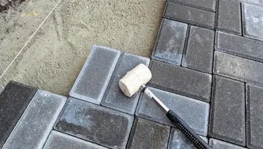 A white rubber mallet used for patio repair lying on a stone patio as it is in the process of having new stones put in.