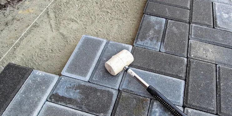 A white rubber mallet used for patio repair lying on a stone patio as it is in the process of having new stones put in.