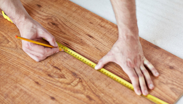 A handyman using measuring tape to measure a section of flooring during a flooring installation project.