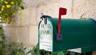 A green mailbox with a red flag placed near the exterior wall of a home after receiving mailbox repair service