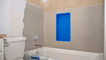 A bathroom remodel in progress, with half of the wall painted above the toilet and unfinished drywall above the bathtub ready for tile installation.