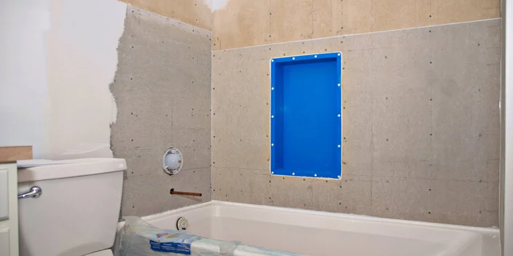 A bathroom remodel in progress, with half of the wall painted above the toilet and unfinished drywall above the bathtub ready for tile installation.