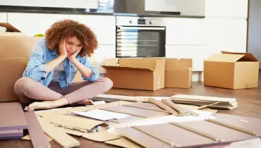 Black woman sitting cross-legged in front of cabinet parts