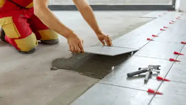 A pro handyman/tiler places ceramic floor tiling in position over adhesive with lash tile leveling system.