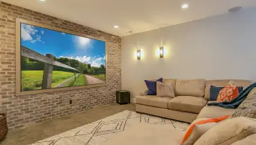 A newly completed basement remodel in Collinsville, IL with new flooring, wall lighting, and a wall-mounted TV.