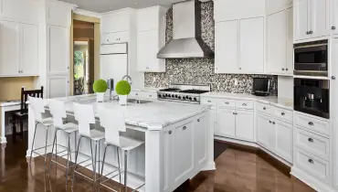 A completed kitchen remodel with a new black and white mosaic backsplash, white cabinets and new wood flooring.