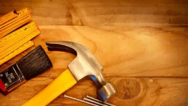 Basic tools used for completing common home repair jobs laid out on top of wooden flooring planks.
