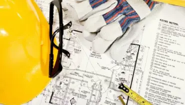 Safety glasses, gloves, and a hard hat on top of the schematics and plan for a home remodeling project.