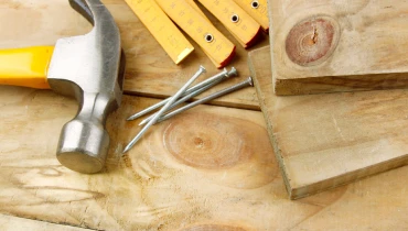A hammer, nails and replacement wooden floorboards on top of wooden surfaces that require floor repairs.