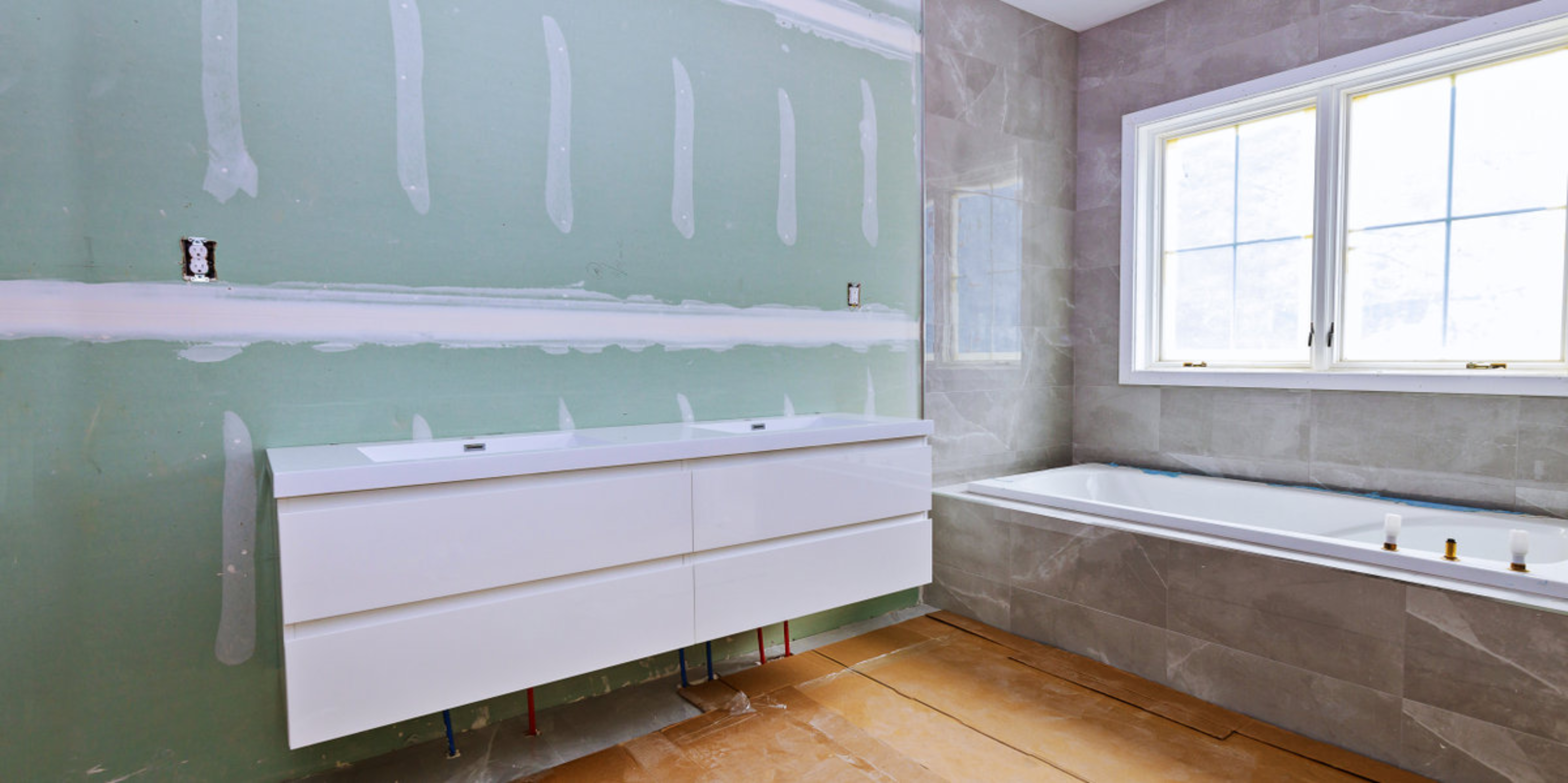 An ongoing bathroom remodeling project, with a storage unit installed on unfinished drywall next to a finished bathtub.
