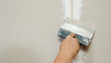 A handyman using a putty knife to smooth out joint compound on a wall during an appointment for drywall repair in Oklahoma City.