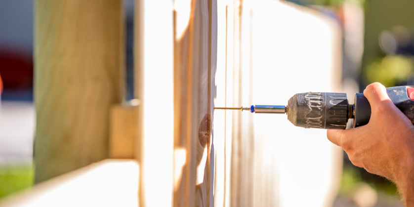 A handyman using a drill to complete fence installation for a new wooden fence.