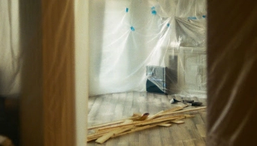 A residential kitchen covered with plastic sheets and filled with wooden planks being used for a home remodeling project.