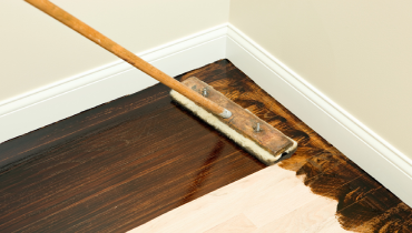 Applying a dark stain with a paintbrush on new oak hardwood floor.