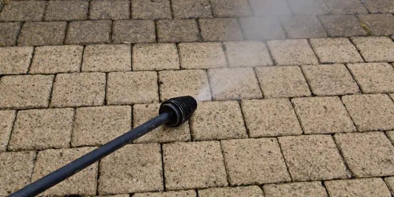 Pressure washing equipment shooting a stream of water over a stone surface that has been partly cleaned.