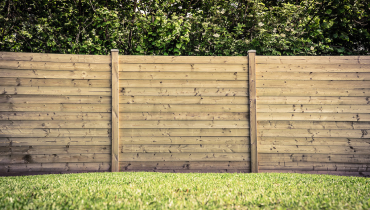 A wooden fence with a natural color after it has been built on a lawn using professional fence installation service.
