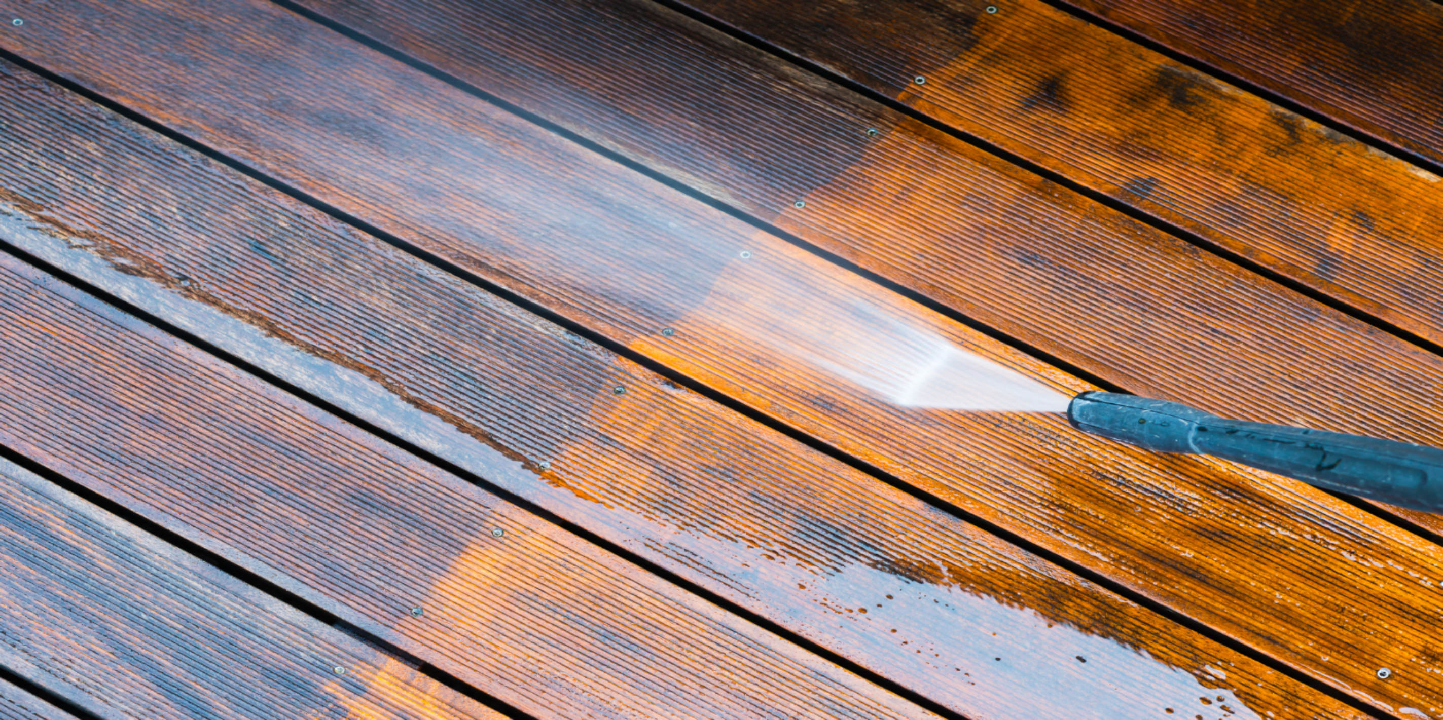The wood of a deck being pressure washed, with one half already done and the other in the process of being washed.