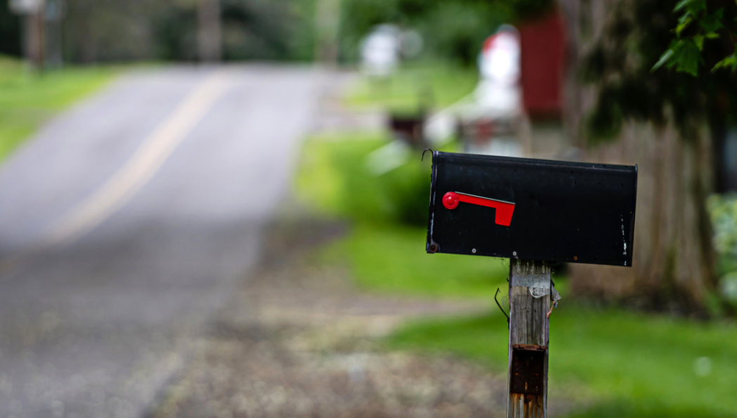 A black mailbox with a red flag and a wooden post that has some minor damage which could be fixed with an appointment for mailbox repair service.