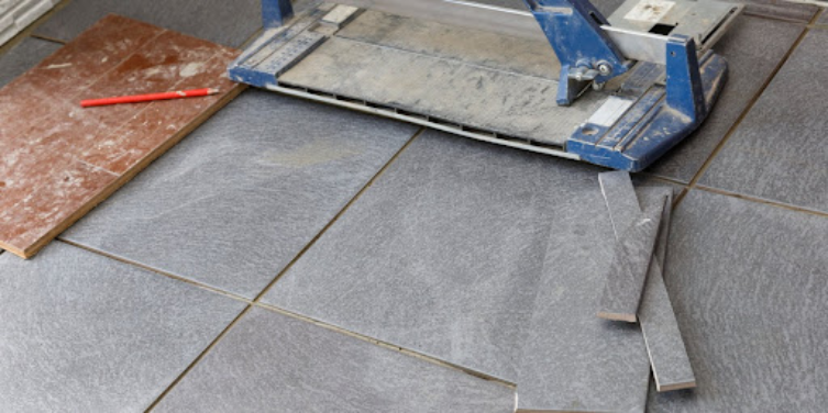 Tools and different-sized pieces of gray tile ready to be used for tile repair on a residential tile floor.
