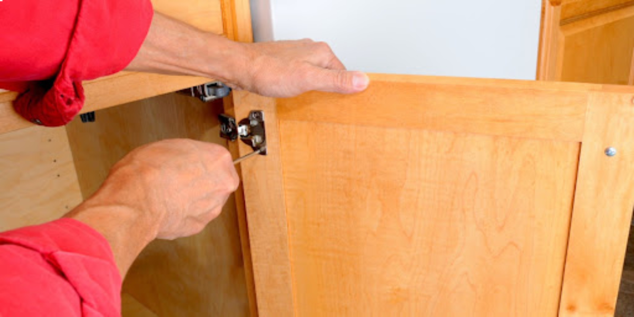 A handyman using a screwdriver to fix hinges on the cabinet doors in a residential kitchen.