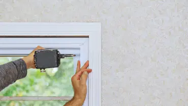A man using a drill to finish installing a window in a frame during an appointment for window repair.