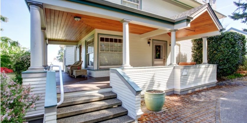 A well-maintained porch with stairs, handrails, and columns on the front of a two-story home.