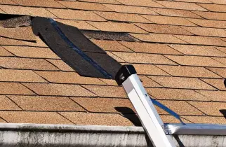 A residential roof with damaged shingles and a ladder placed nearby for workers to access the roof and complete roof repairs.