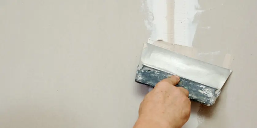 Drywall repairs being finished with a putty knife.