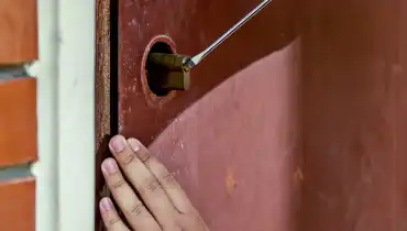 A handyman using a screwdriver to complete door repairs for the locking mechanism of a residential door.