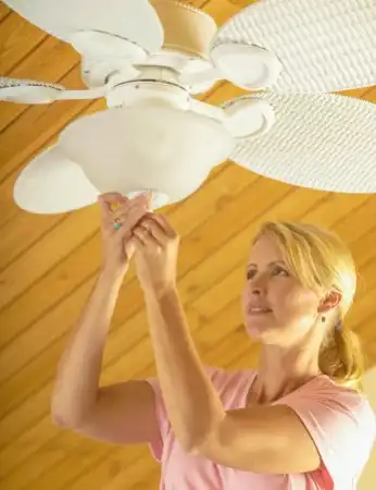 Homeowner installing white ceiling fan.