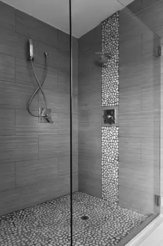 A shower with glass door and gray tiles.