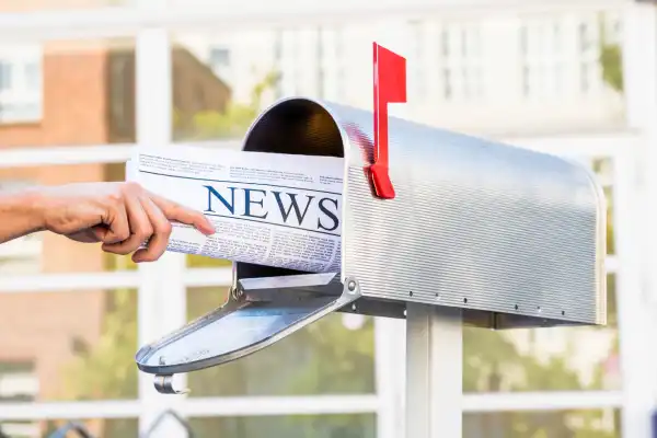 Hand pulling newspaper from metal mailbox.
