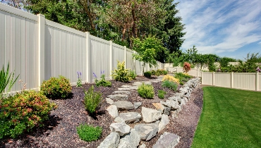 A backyard bordered by a white fence after new fence installation has been completed.