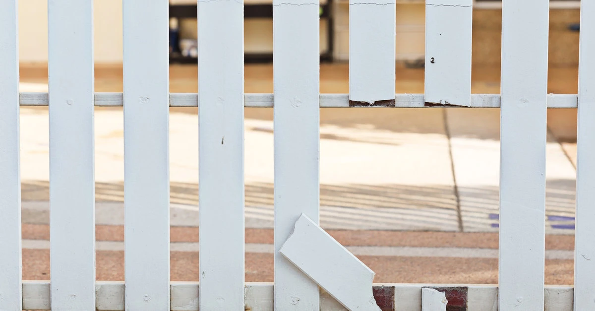 A white picket fence with broken pickets creating a hole that must be fixed with fence repair services.