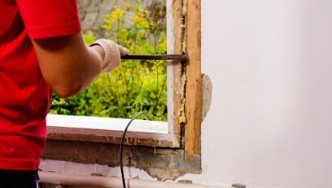 A handyman using a crowbar to remove a window from its frame before installing a replacement window.