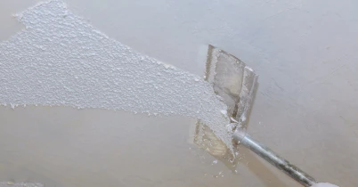 A handyman using a scraper to remove the textured drywall from a ceiling during a popcorn ceiling removal project.