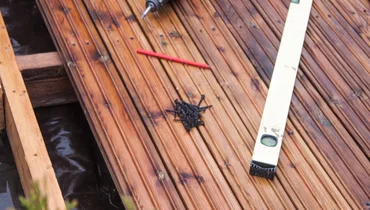 A level, nails, and a pencil lying on top of a wooden deck undergoing deck repairs that involve replacing boards.