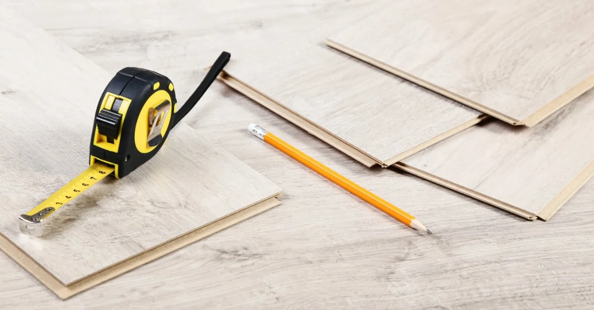 A tape measure, pencil and several laminate floor boards laid out across a large laminate floor before being used for floor repair in Cincinnati, OH.