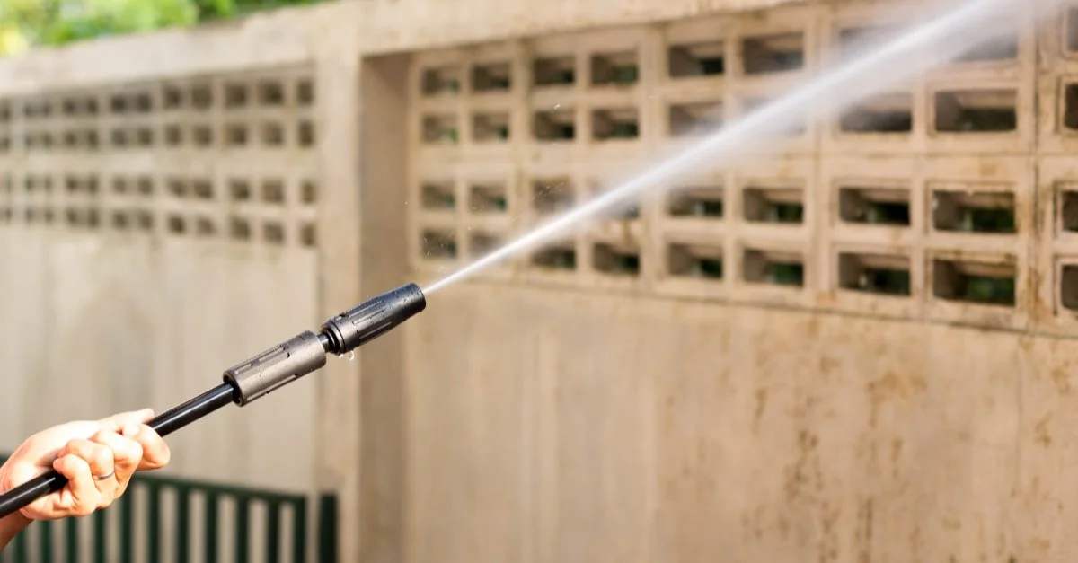 A pressure washer shooting out a jet of water as a person uses it while pressure washing a dirty fence.