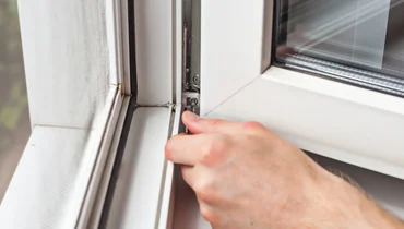 A handyman performing window repairs by using a hex key to adjust the bottom latch on a casement window.