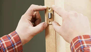 A handyman using a screwdriver to install a new lock and door knob assembly during an appointment for door repair.