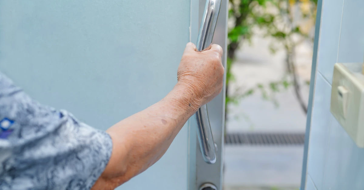 An eldery person gripping a long door handle installed in their home as an aging-in-place modification.