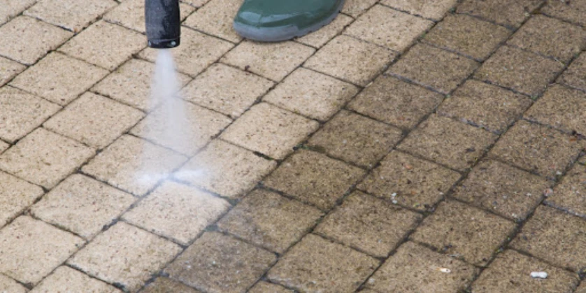 A pressure washer cleaning outdoor tiles, with a straight line separating the area where the tiles have been cleaned and the darker area where they are still dirty.