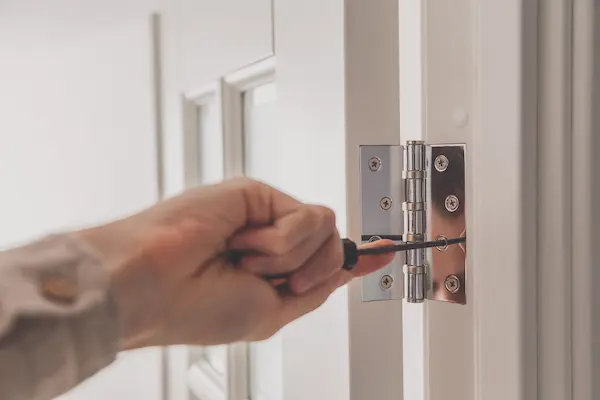 A hand tightening a door hinge.
