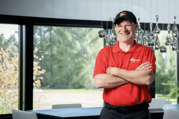 A Mr. Handyman service professional stands in front of a window