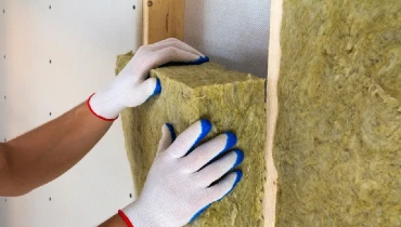 Closeup of a person wearing white gloves applying insulation to an interior wall.